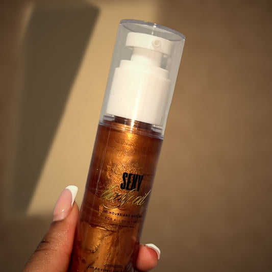 Her hand holding the Sexy body oil in warm window light, the bottle's shadow falling across a sunlit plaster wall